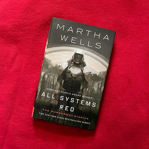 A picture of the book All Systems Red by Martha wells (a greyscale image of a human-shaped "security unit" in armour) on a red background