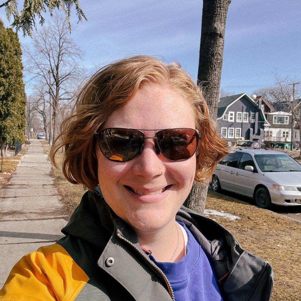 A selfie of the author with a very cute wavy bob. She's outside wearing sunglasses and her Star Wars rain jacket.