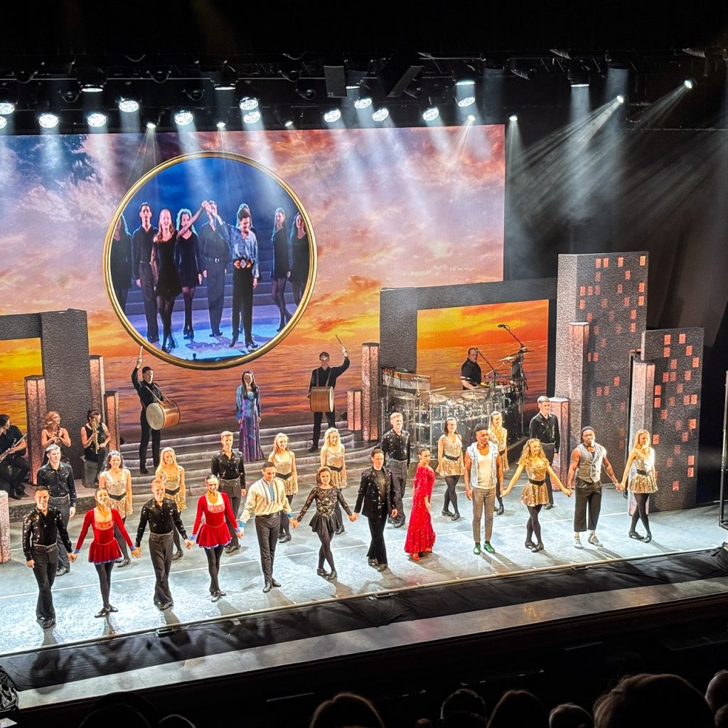 The cast of Riverdance lined up for bows in back, fold, and red costumes